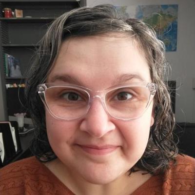 a photo of a woman with brown and gray hair, clear glasses, and a brown sweater